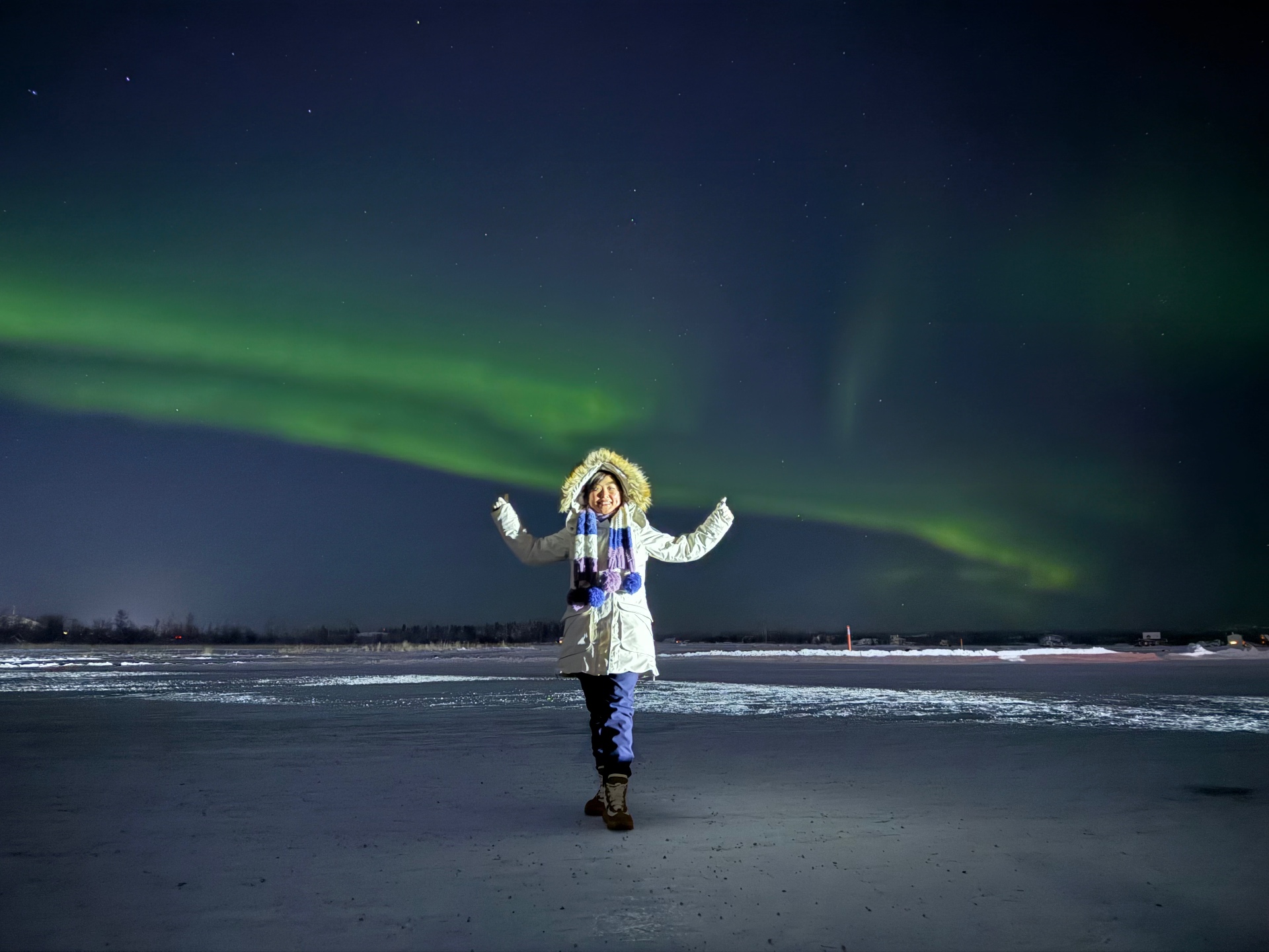 Happy visitor under aurora on frozen lake